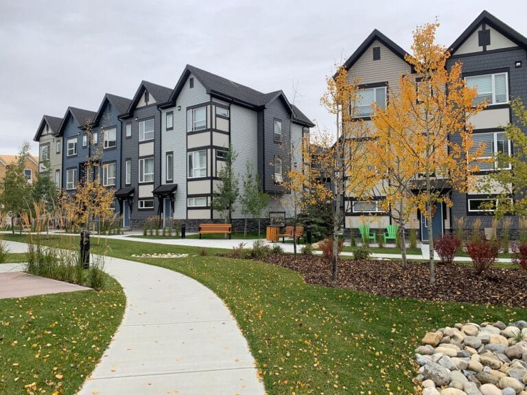 A row of three storey townhouses beside a path lined with autumn trees