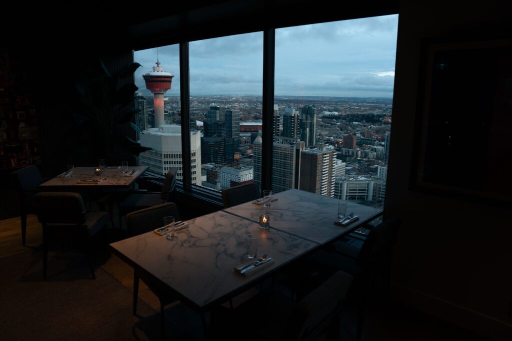 A city view through large windows from a warmly lit interior