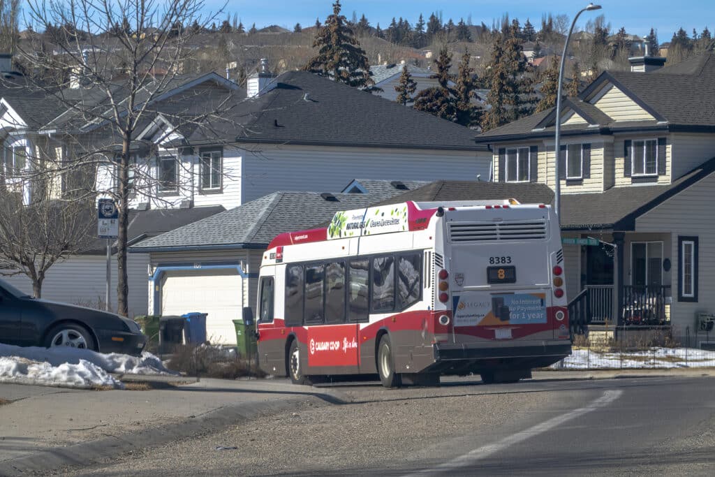 A Calgary Transit bus on a quiet residential street lined with detached homes