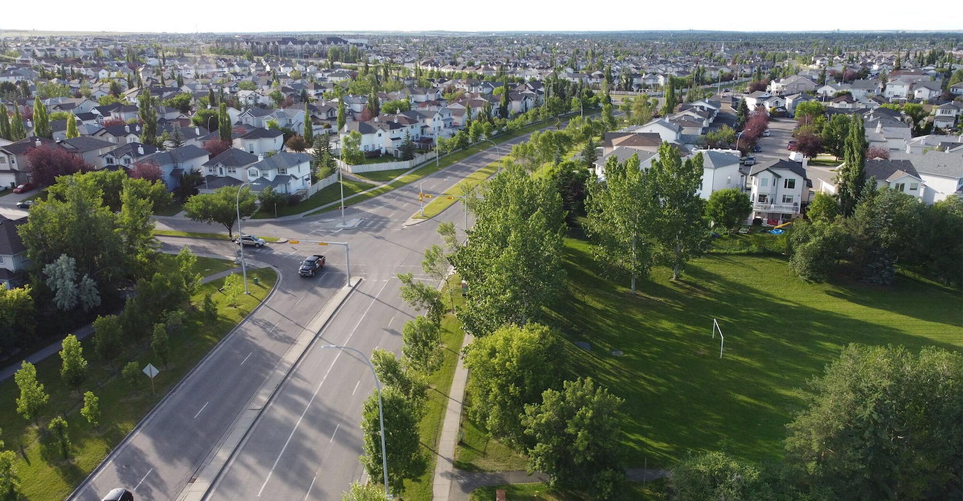 Aerial view of a green Calgary suburb with parkland and a divided road