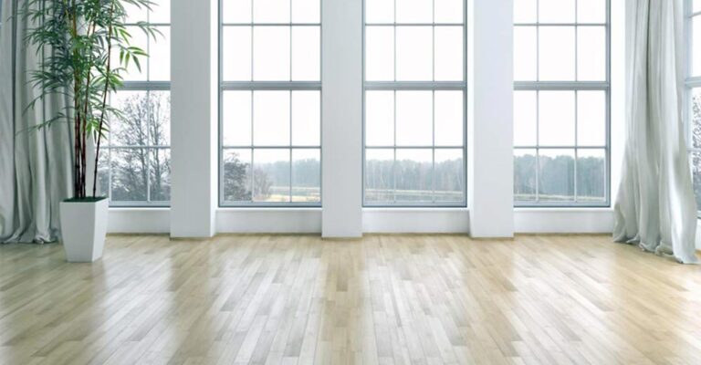 An empty, bright living room with tall windows and a light wood floor