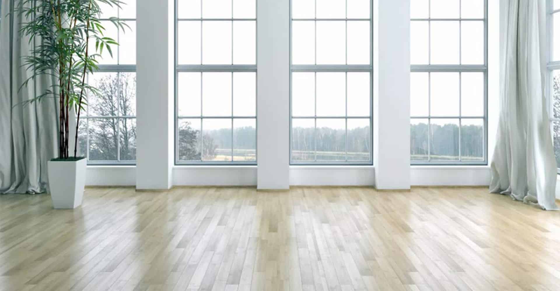 A bright empty living room with tall windows and light wood floors