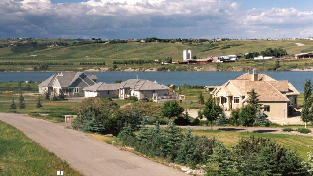 Acreage homes beside the water in Rocky View County, Alberta, with rolling hills behind